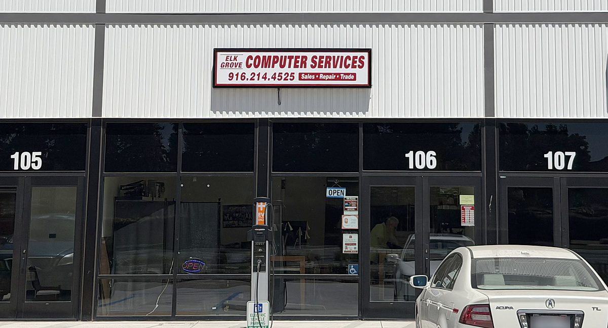 The shop from the parking lot: a red and white sign reading Elk Grove Computer Services, 916.214.4525, Sales, Repair, Trade, mounted above the glass storefront of Suite 106, with Suite 105 to the left and Suite 107 to the right.